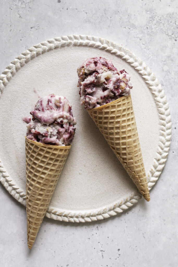 two ice cream sugar cones filled with blackberry cobbler ice cream laying on a plate.