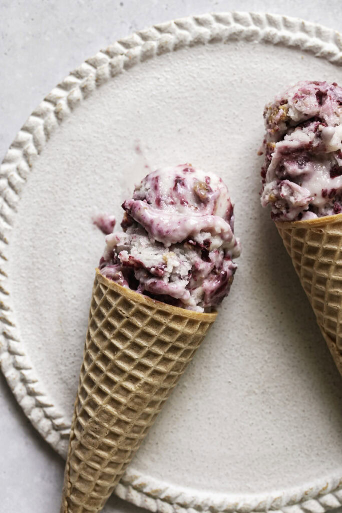 close up image of two ice cream sugar cones filled with blackberry cobbler ice cream laying on a plate.