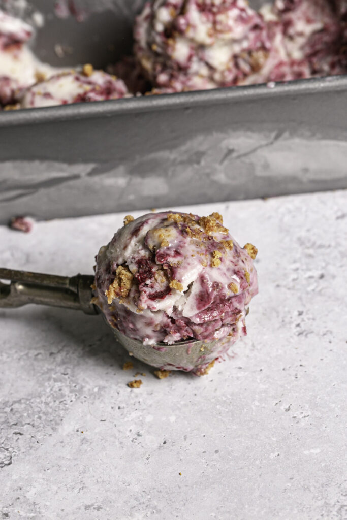 a scoop of blackberry cobbler ice cream in an ice cream scooper in front of a loaf pan of blackberry cobbler ice cream.