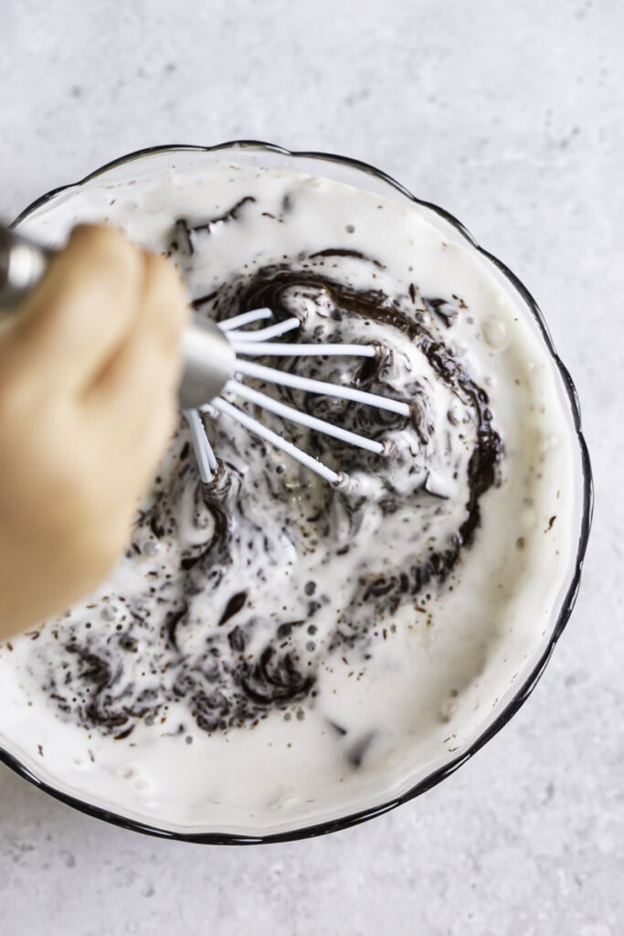 action shot stirring the hot coconut milk with the melted chocolate chunks with a whisk.