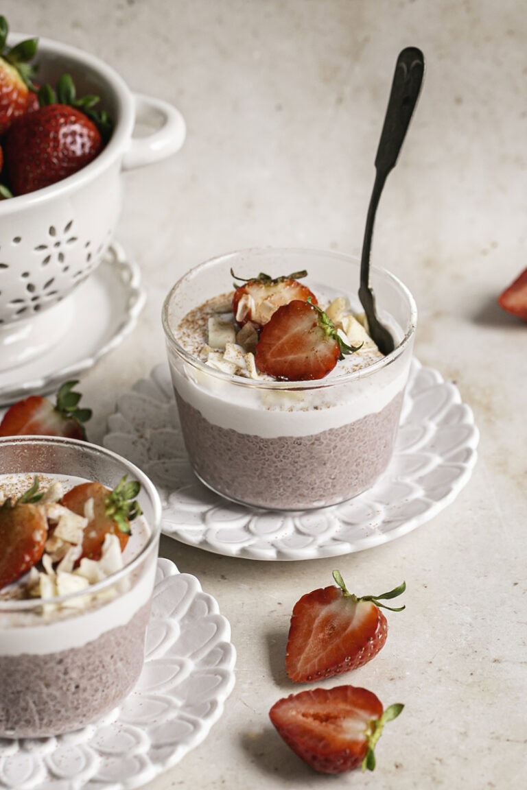 two glasses of strawberry hibiscus chia seed pudding, and a small berry strainer filled with fresh strawberries.
