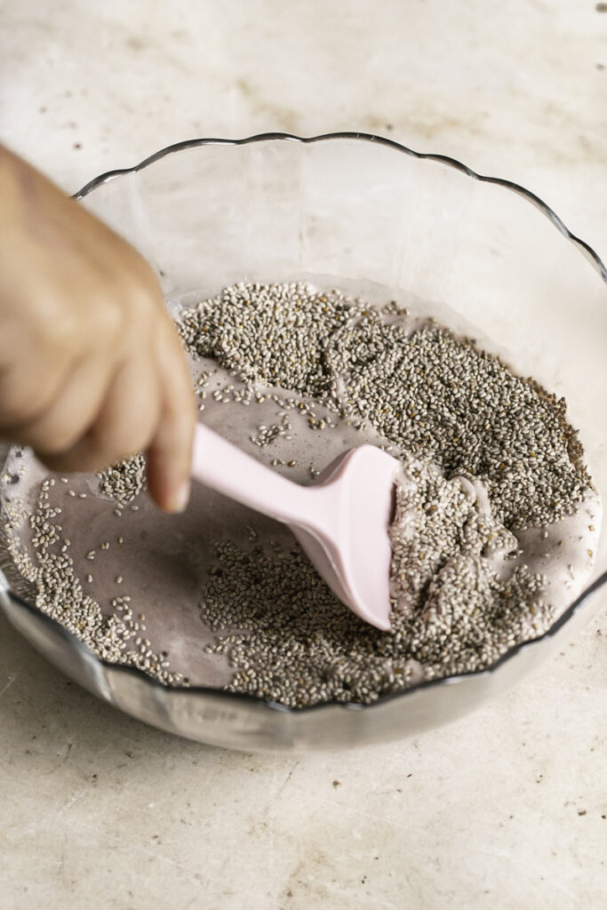 action shot of a small pink spatula stirring the chia seeds with the strawberry hibiscus milk.