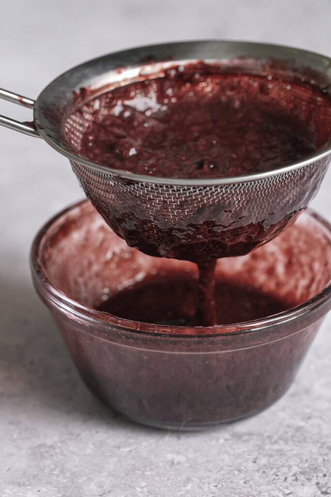 straining blackberry curd through a fine mesh strainer into a glass bowl.