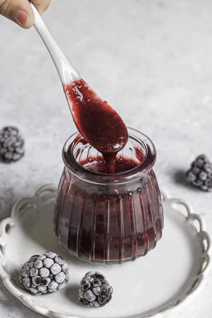 blackberry curd in a small glass jar with a spoon drizzling some back into the jar.