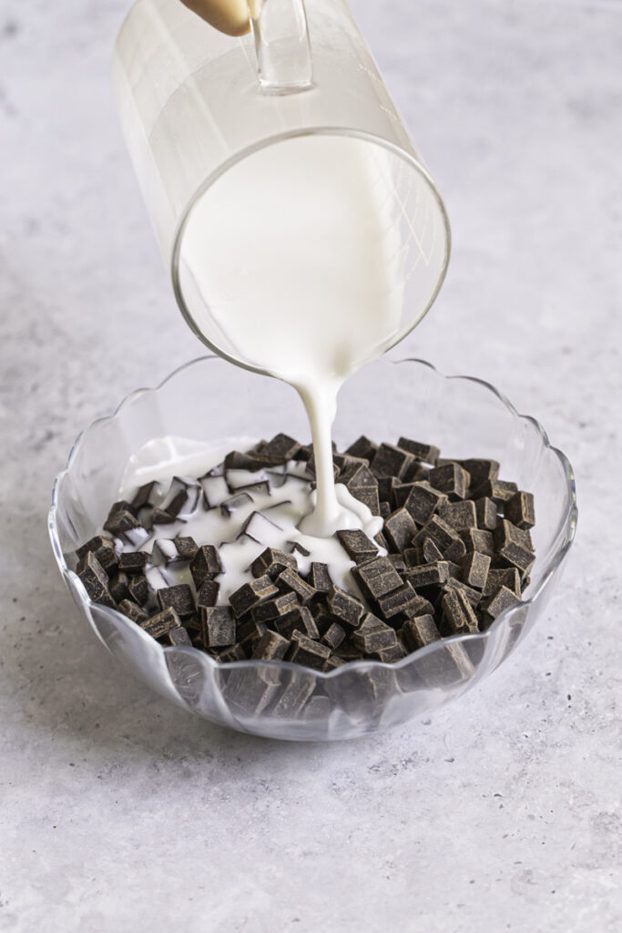 action shot of pouring hot coconut milk over a bowl of chocolate chunks.