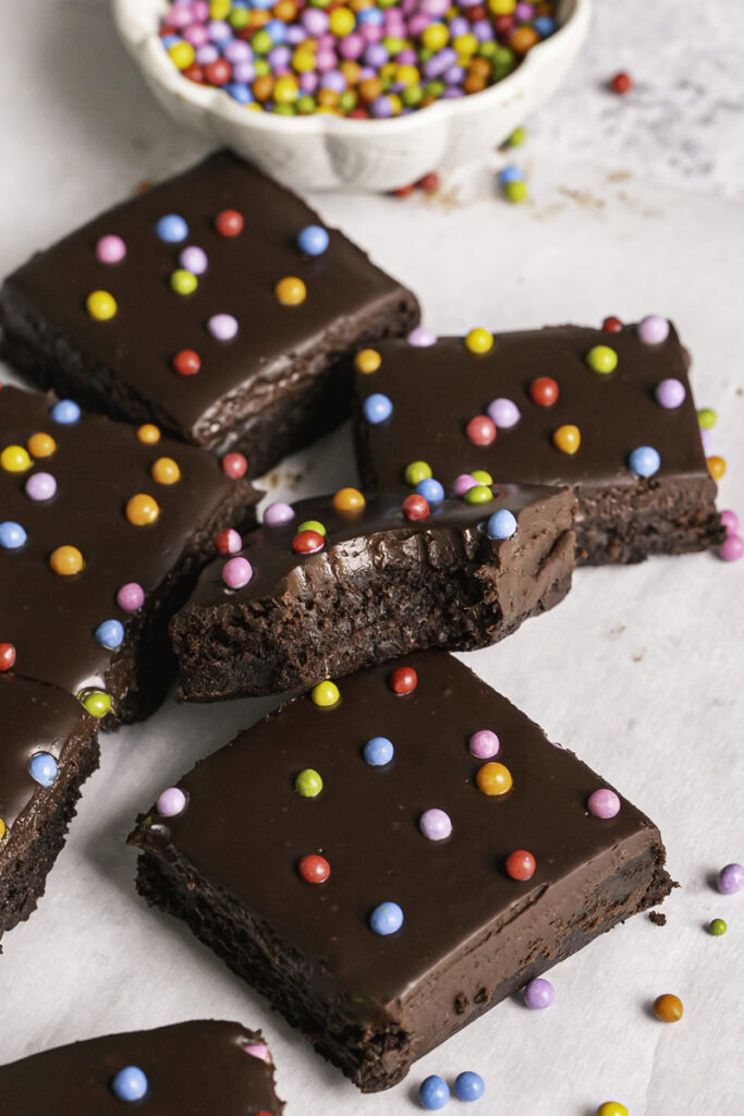 sliced cosmic brownies on a piece of parchment paper and a bowl of rainbow sprinkles in the background.