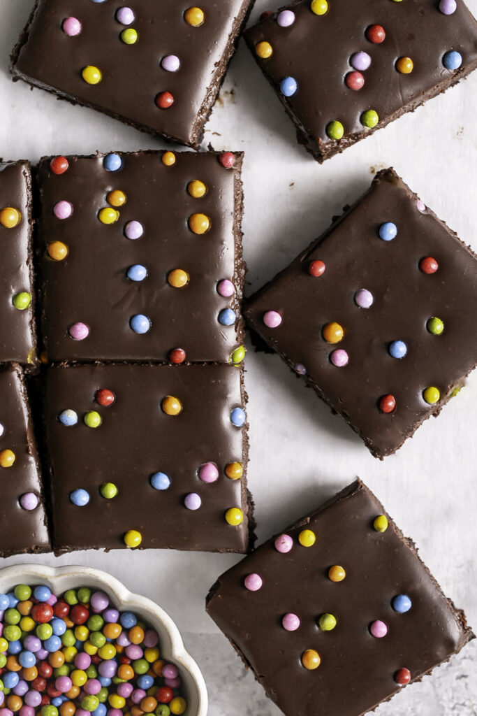overhead sliced cosmic brownies with a small bowl of rainbow chocolate chips in the lower left corner.