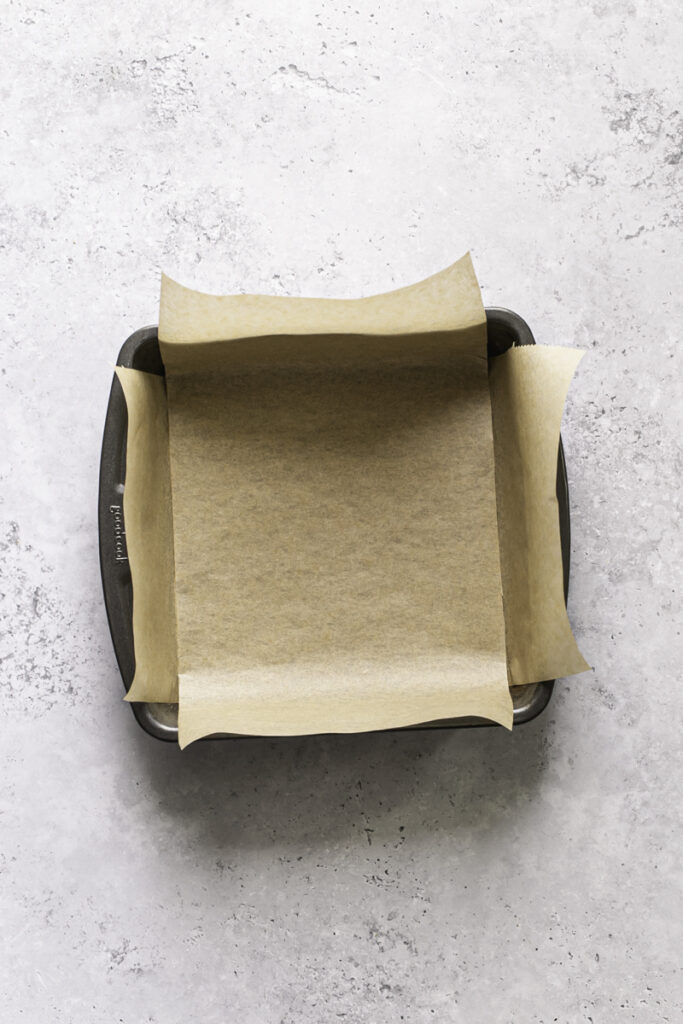 overhead shot of an 8x8 square baking pan lined with parchment paper.
