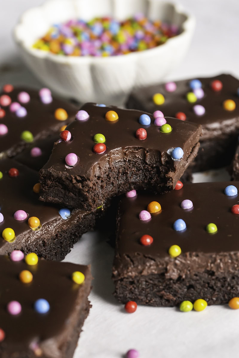 close up of sliced cosmic brownies on a piece of parchment paper and a bowl of rainbow sprinkles in the background.
