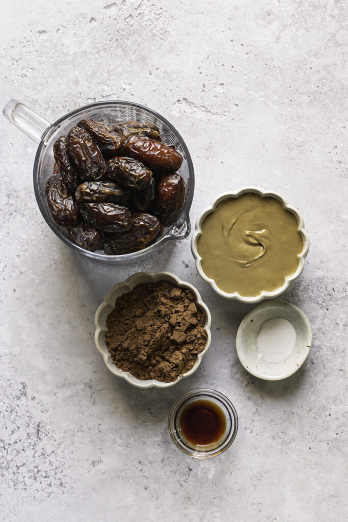 the 5 ingredients needed to make date brownies: dates, sunflower seed butter, cacao powder, baking soda, pure vanilla extract.