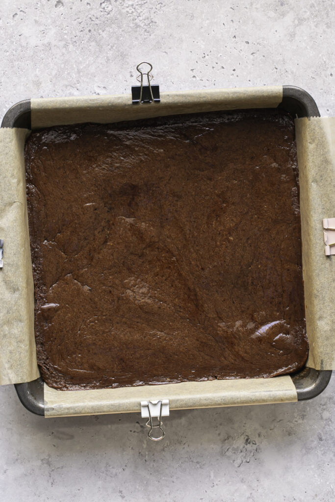 the unbaked date brownie batter pressed into a square parchment-lined baking pan.