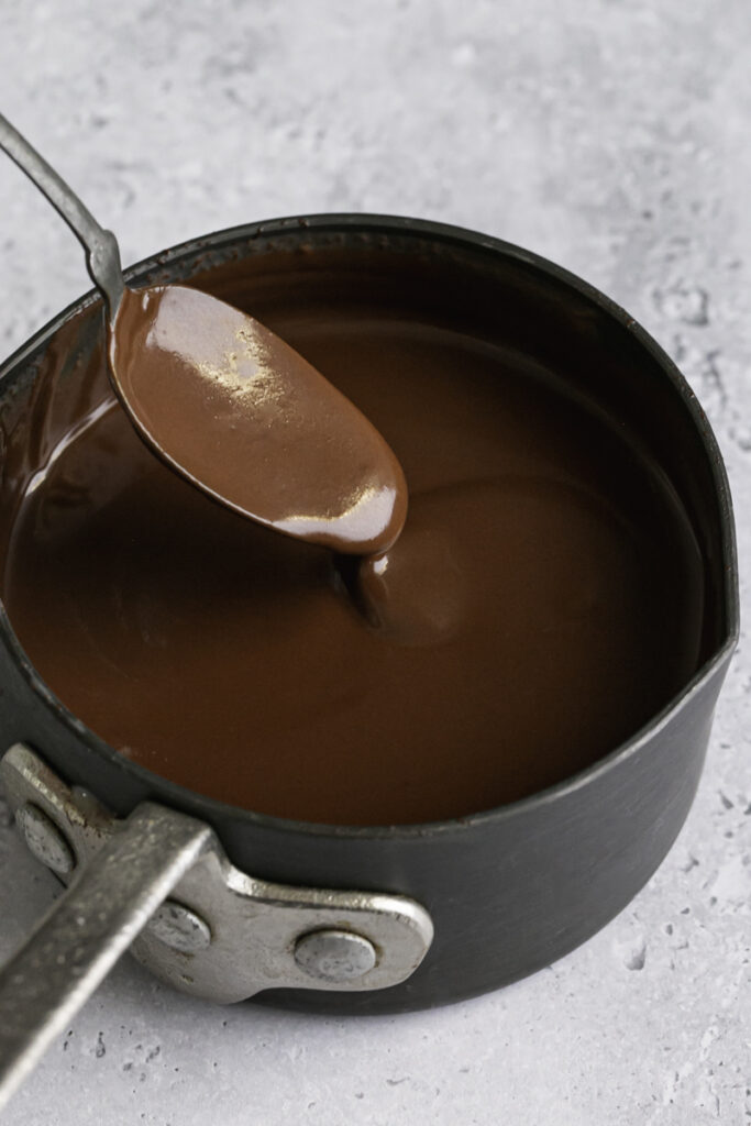 melted smooth and silky chocolate in a small saucepan with some chocolate drizzling off a spoon in to the pan.