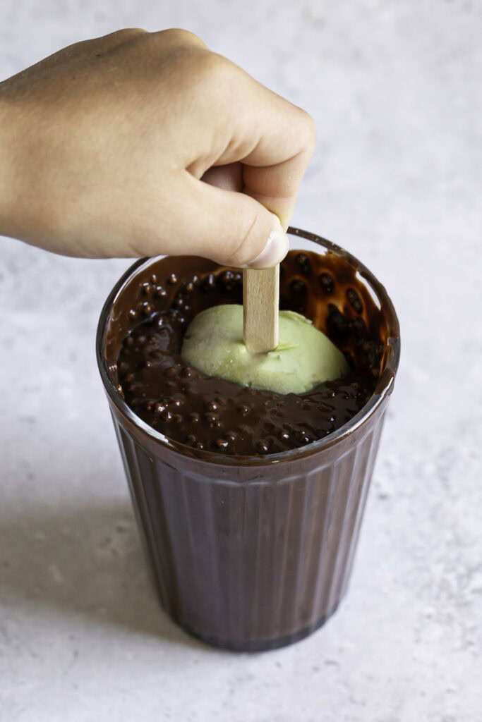 a hand dipping the creamy avocado mint chocolate ice cream bar in the melted chocolate.