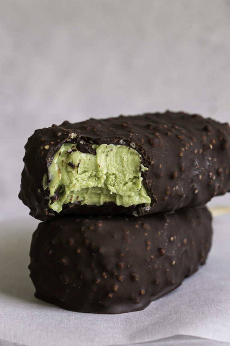 two creamy avocado mint chocolate ice cream bars stacked on top of one another, the top one with a bite taken out of it.