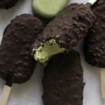 creamy avocado mint chocolate ice cream bars piled on top of one another, one not coated in chocolate and the top one with a bite taken out of it.