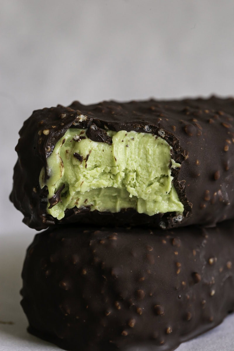 two creamy avocado mint chocolate ice cream bars stacked on top of one another, the top one with a bite taken out of it.