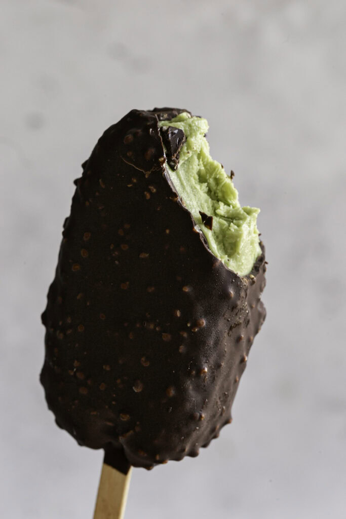 a single creamy avocado mint chocolate ice cream bar with a bite taken out of it.