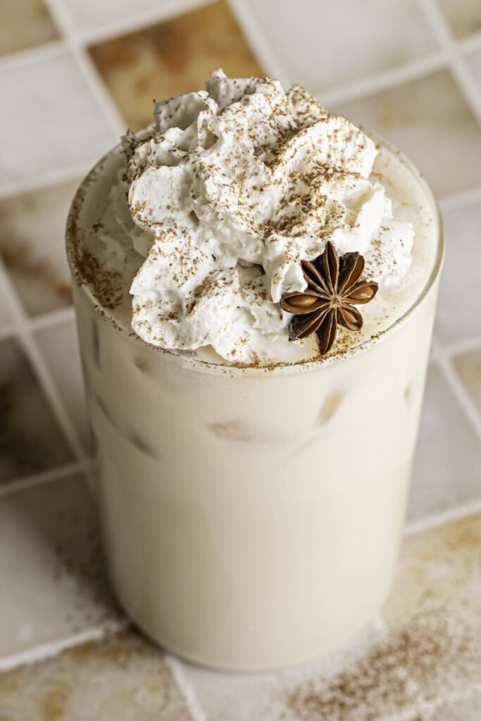 a 3/4 shot of a glass of iced oatmilk chai latte with whipped cream on top.