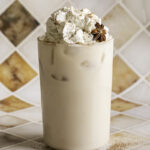 a glass of iced oatmilk chai latte with whipped cream on top.