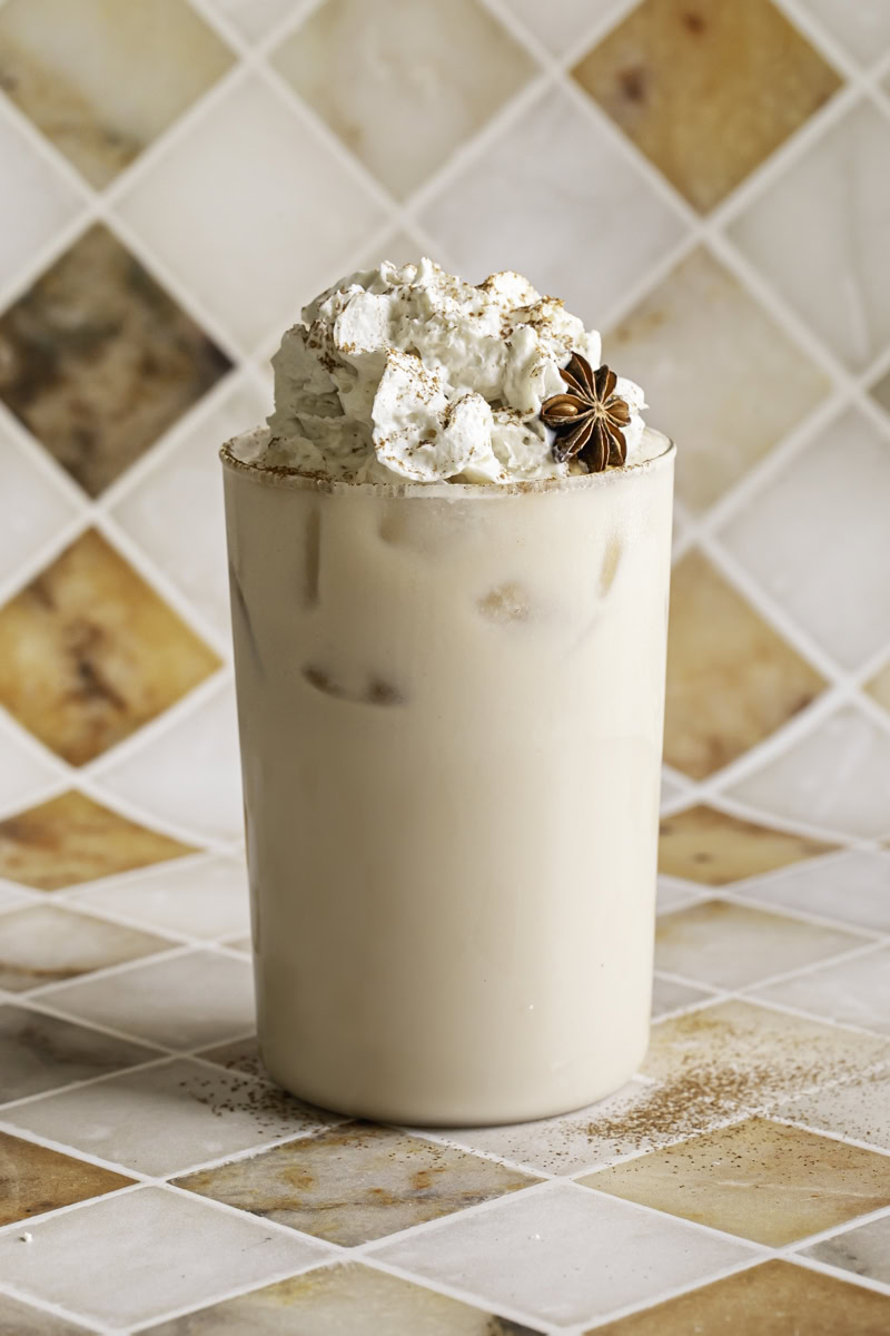 a glass of iced oatmilk chai latte with whipped cream on top.
