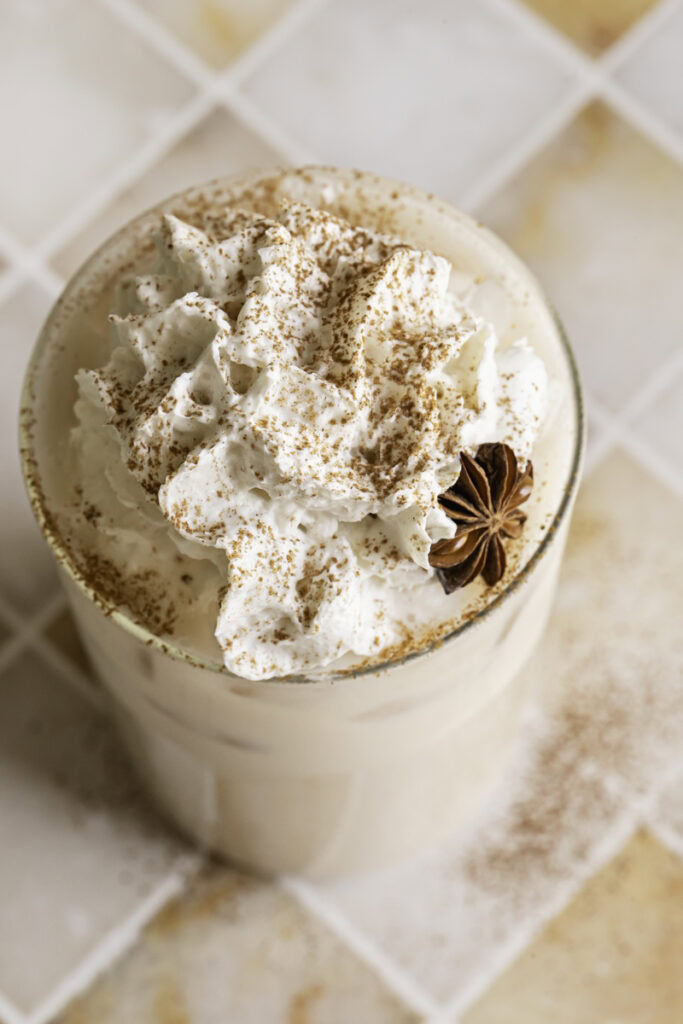 overhead shot of a glass of iced oamilk chai latte with whipped cream and sprinkled with cinnamon.