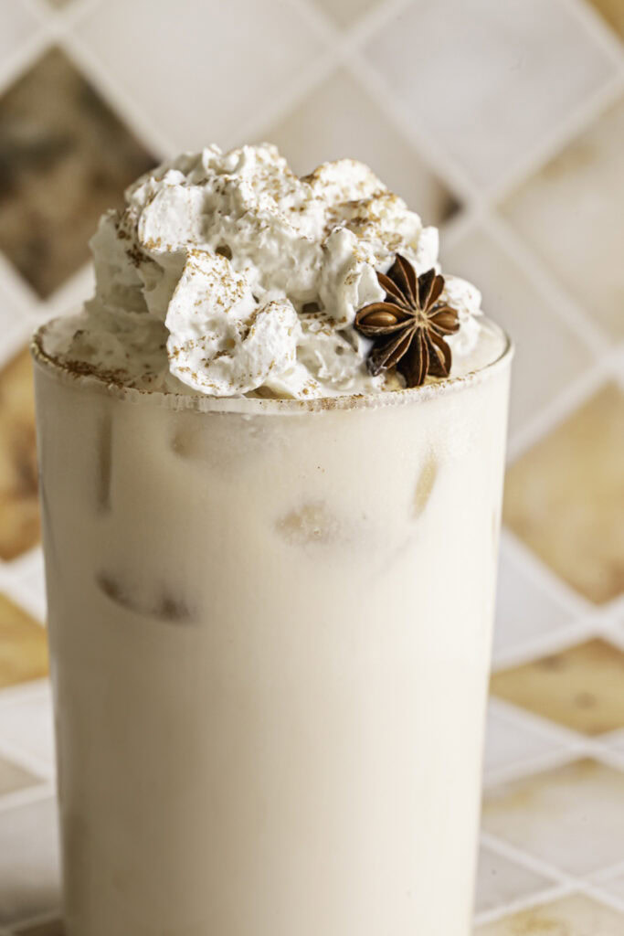 a close up shot of iced oatmilk chai latte with whipped cream.