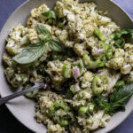 a bowl of Low Carb Roasted Cauliflower Potato Salad with a spoon sticking out of the bowl on a blue backdrop.