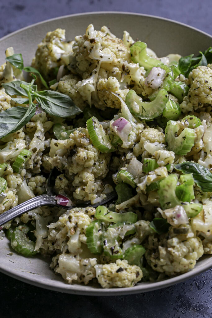 3/4 close up of Low Carb Roasted Cauliflower Potato Salad with a spoon sticking out of the bowl.