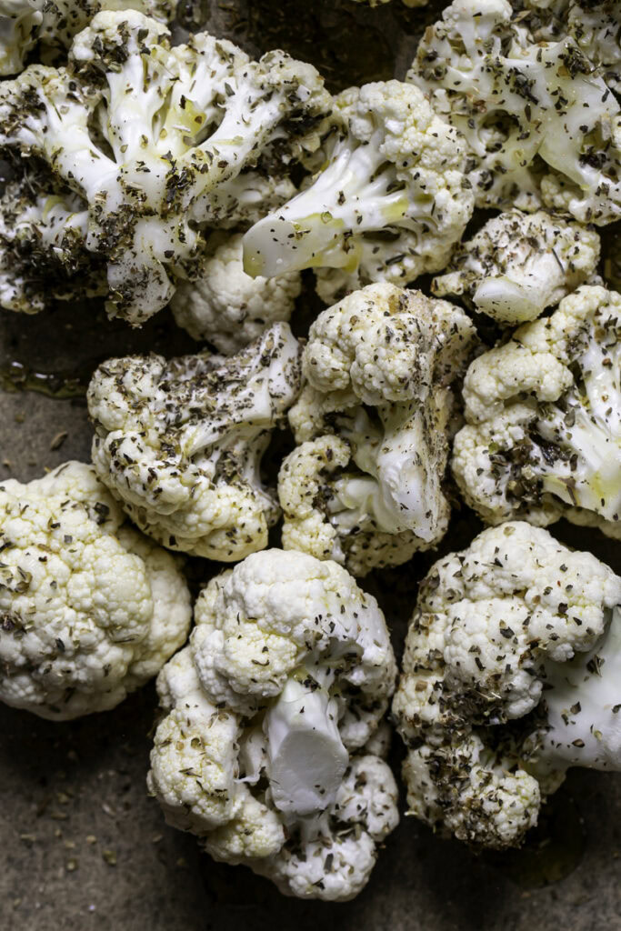 cauliflower florets tossed in olive oil and herbs on a parchment-lined baking sheet.