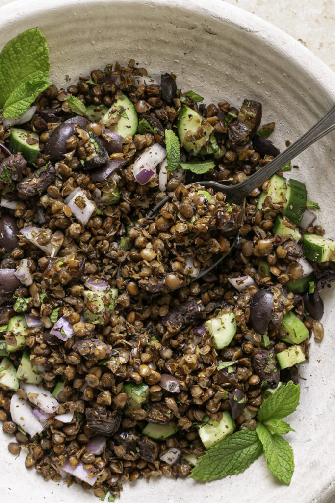 close up of tossed roasted lentil greek salad in a large bowl with a spoon in it.