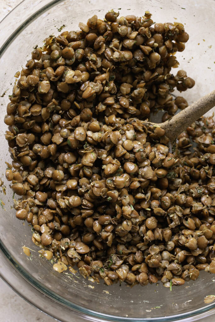 lentils mixed with greek spices in a glass bowl with a spoon in the bowl.