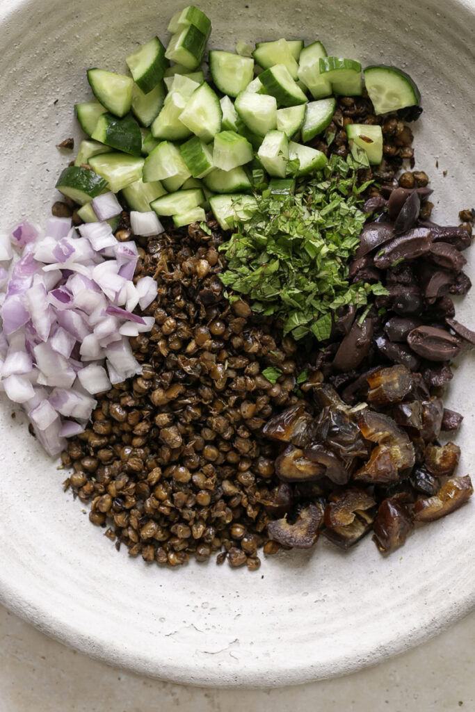 all of the roasted lentil greek salad ingredients unmixed in a large bowl.