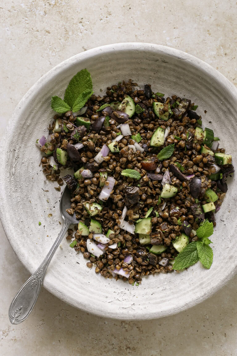 a bowl of roasted lentil greek salad in a large bowl with a spoon in it.