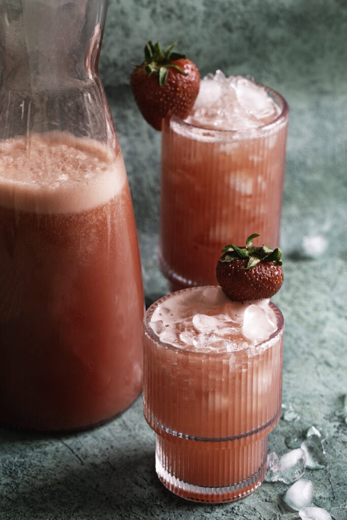 a jug of watermelon strawberry water next to two glasses of watermelon strawberry water poured over ice.