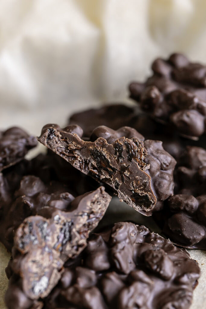 close up of chocolate raisin clusters, one cut in half sitting on another cluster.