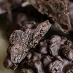 close up of chocolate raisin clusters, one cut in half sitting on another cluster.