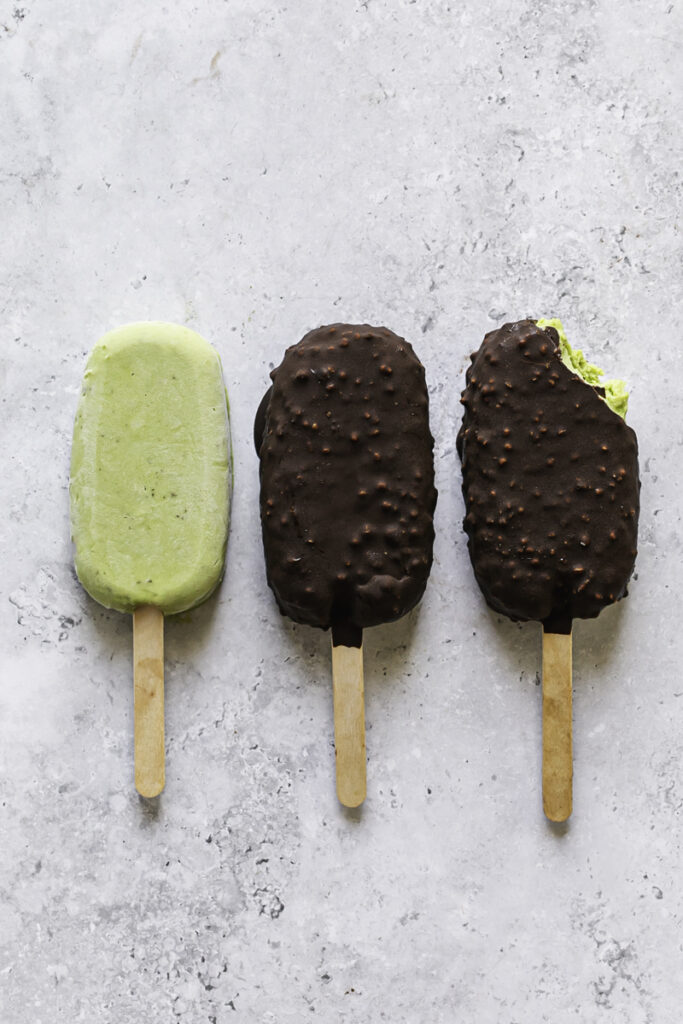 three ice cream bars, the first one not coated in chocolate, the middle one covered in chocolate and the third one covered in chocolate with a bite taken out of it.