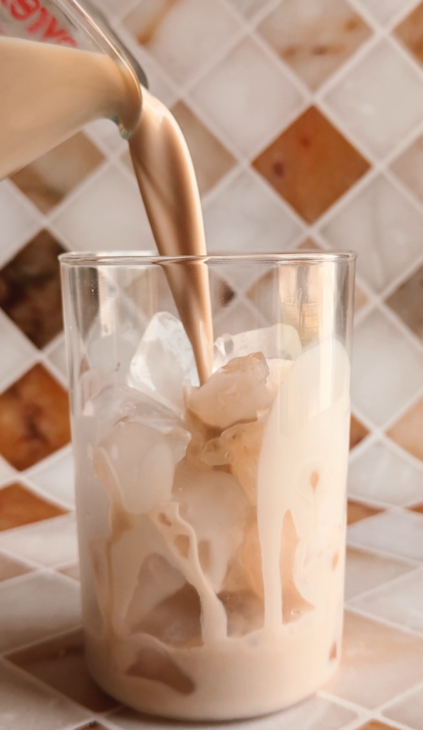 Action shot pouring the Oatmilk chai latte in a glass filled with ice.