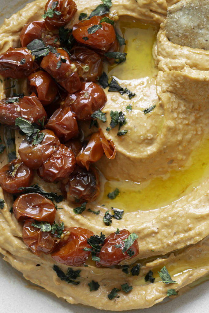 a close up image of a bowl of roasted cherry tomato hummus garnished with roasted cherry tomatoes.