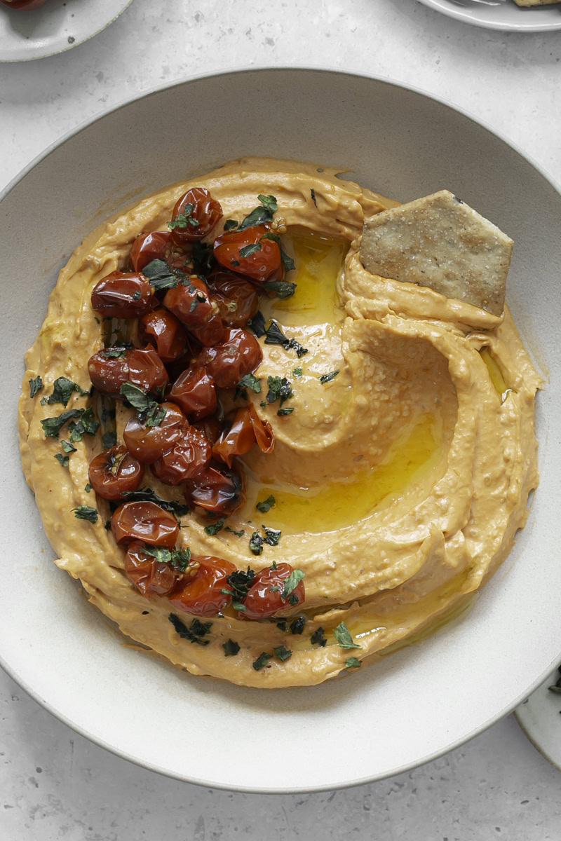 a close up image of a bowl of roasted cherry tomato hummus garnished with roasted cherry tomatoes.