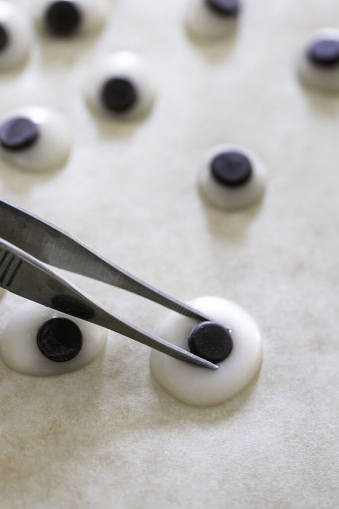 action shot placing the mini chocolate chip pupil in the white chocolate with culinary tweezers.