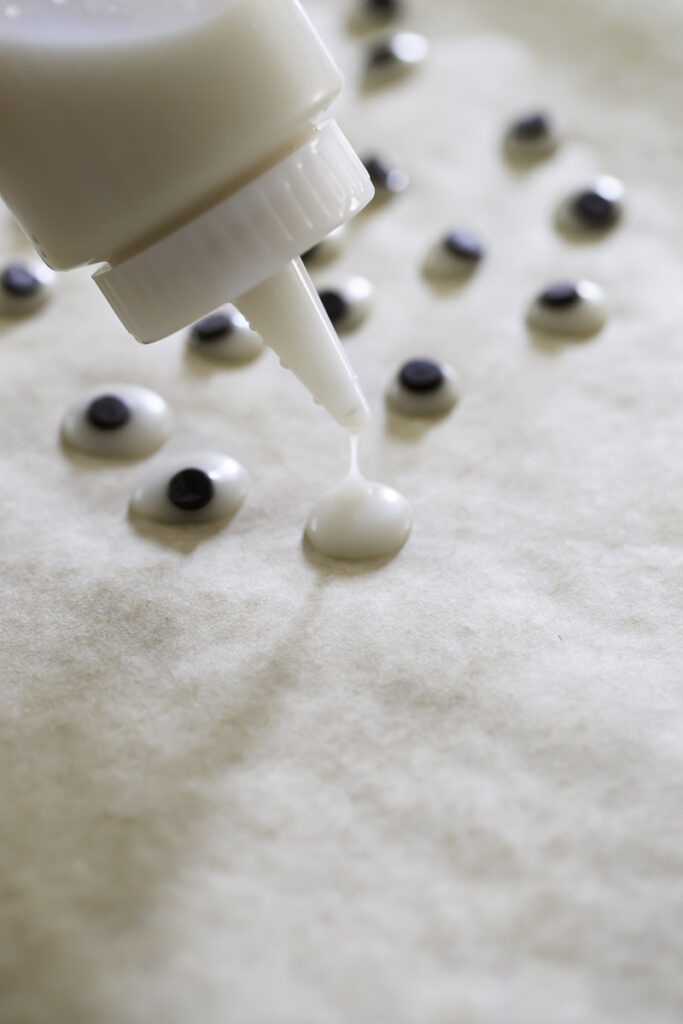 action shot of squeezing melted white chocolate out of a squeeze bottle to make the googly eyes.