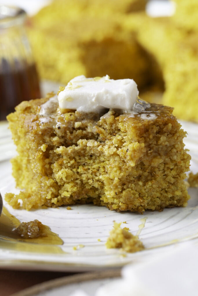 a close up shot of a piece of cornbread with butter on top and a bite taken out of it.