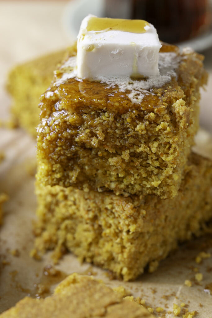 a close up of two pieces of pumpkin cornbread stacked on top of one another with butter and maple syrup on top.