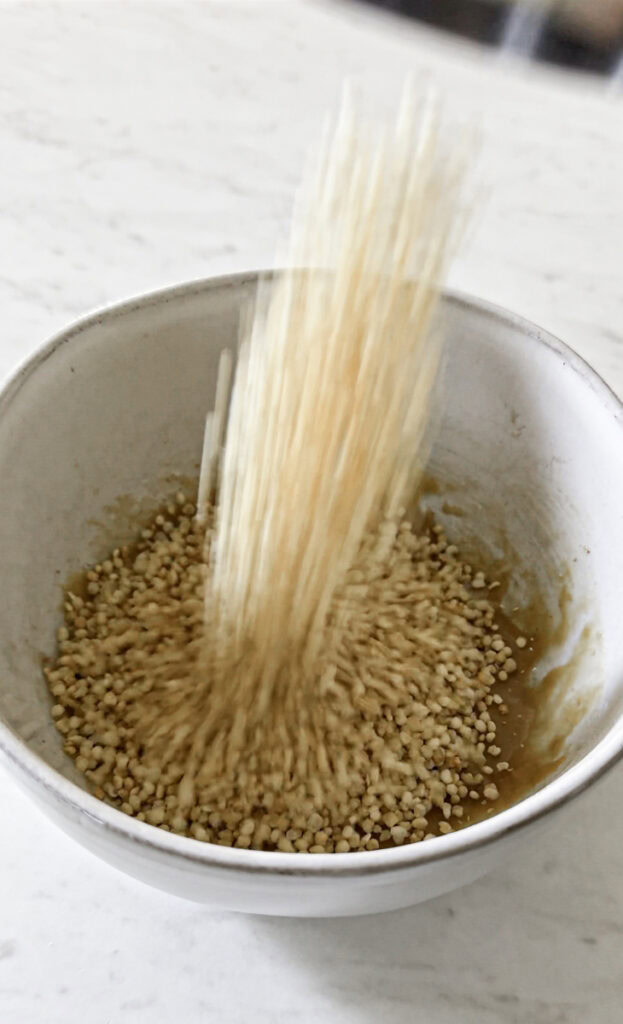 action shot pouring puffed quinoa into the melted peanut butter mixture.