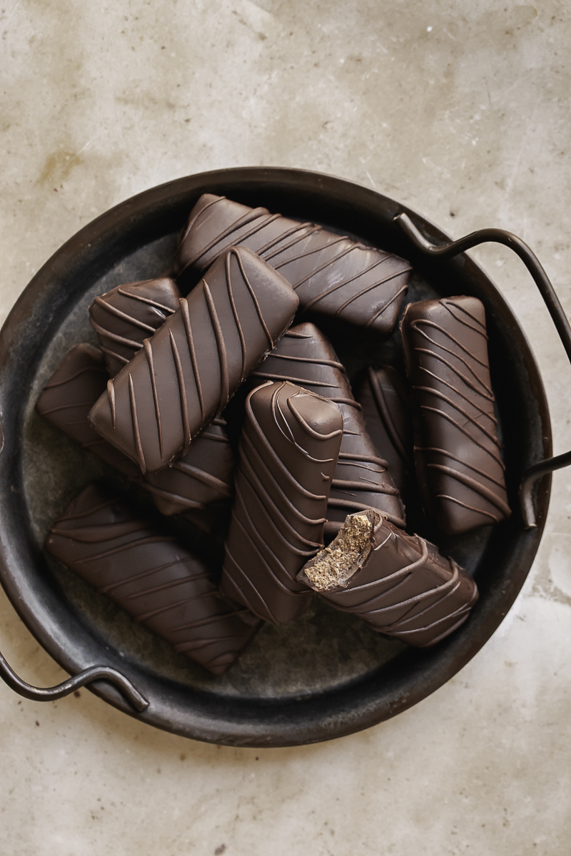 Crispy Peanut Butter Protein Chocolate Candy Bars stacked on a round enamel plate, one of the bars with a bite taken out of it.