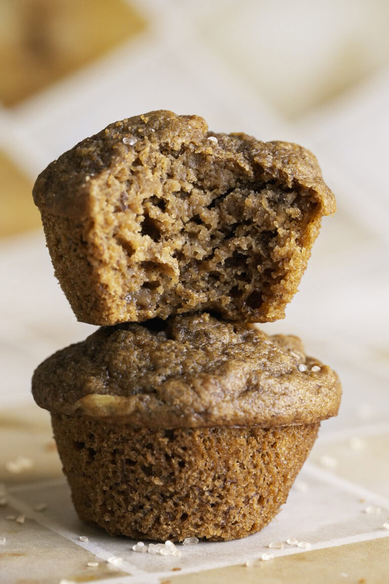 two apple cider banana bread muffins stacked on top of one another, the top muffin with a bite taken out of it.