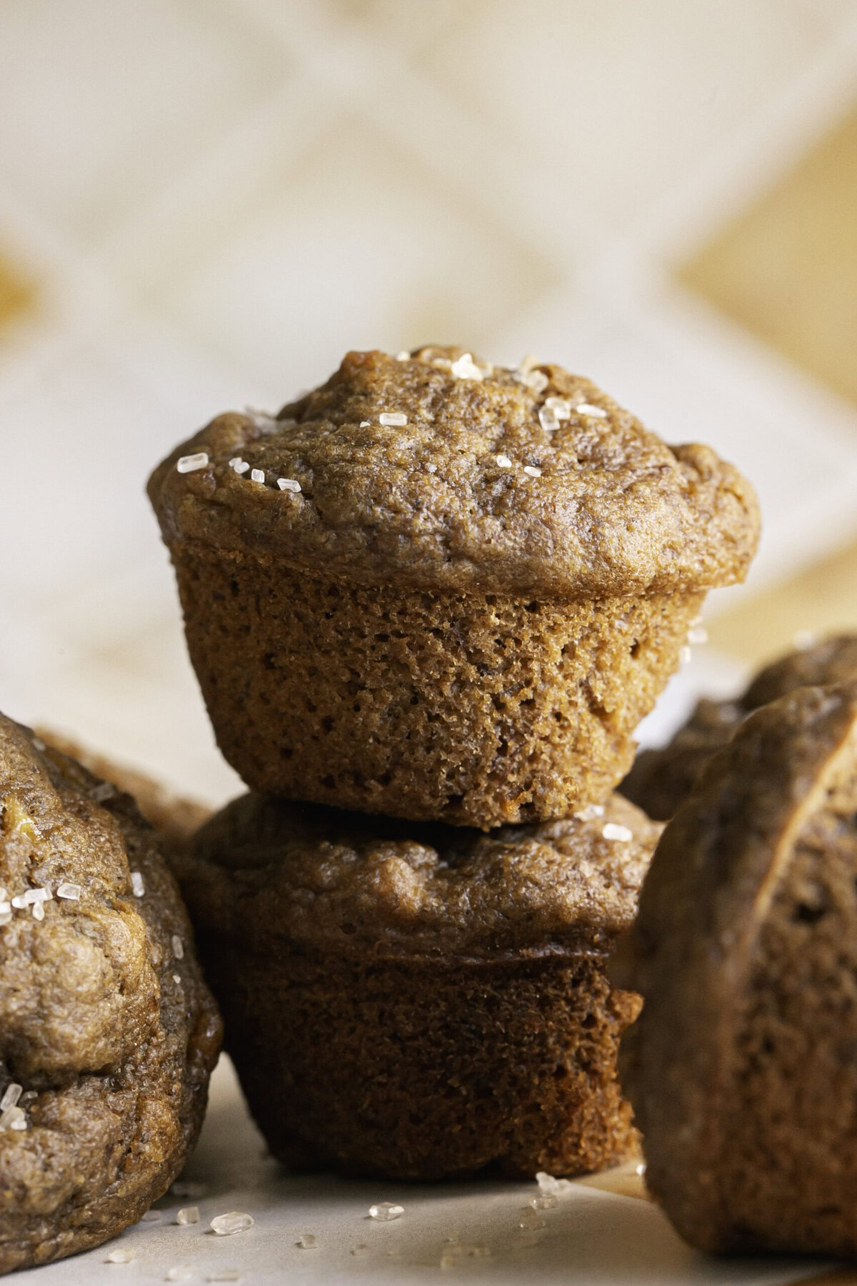 two mini apple cider banana bread muffins stacked on top of one another and other muffins around it.