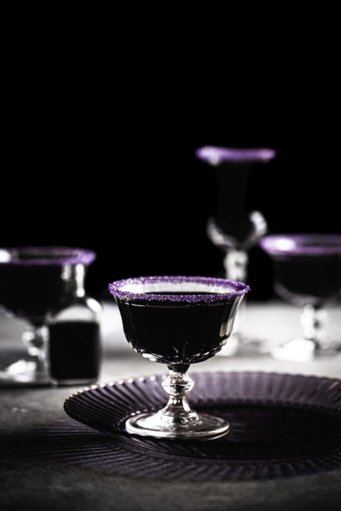 black apple juice mocktails with purple sand sugared rims.