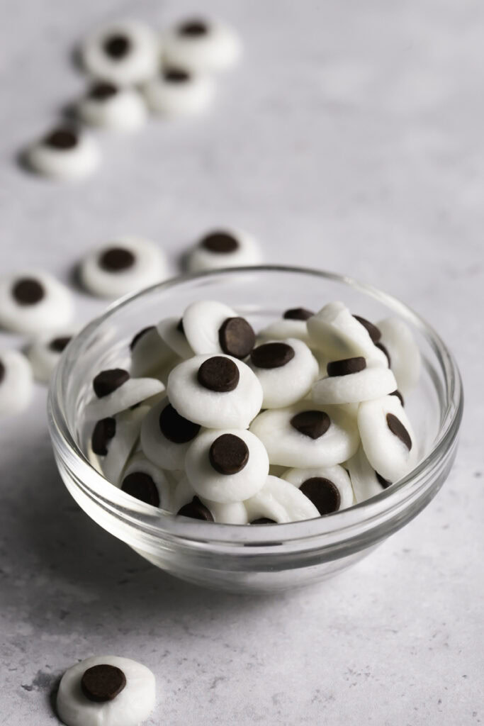 3/4 shot of chocolate candy googly eyes in a small glass bowl with other eyes outside the bowl around it.